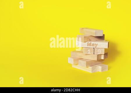 Mai. Tag 19 des Monats, Kalenderdatum. Holzblöcke in den Turm gefaltet mit Monat und Tag auf gelbem Hintergrund, mit Kopieplatz. Frühlingsmonat, Stockfoto