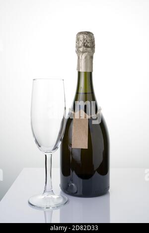 Eine Flasche Alkohol mit einem Etikett auf einer Schnur und ein Glas auf einem hellen Hintergrund. Stockfoto