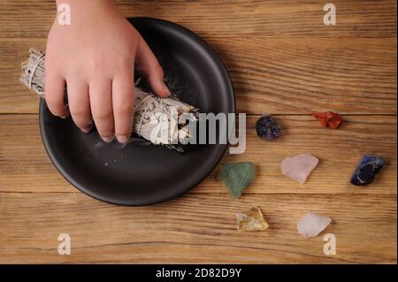 Verschmierendes Ritual mit brennendem Bündel weißen Salbei. Bild mit heilenden Chakra-Mineralsteinen. Reinigen Sie das Haus mit Duftrauch. Stockfoto