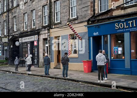 Sozial distanzierte Warteschlange vor dem James Wood & Sons Barber Shop, gegründet 1890, Drummond Street, Edinburgh, Schottland, Großbritannien. Stockfoto