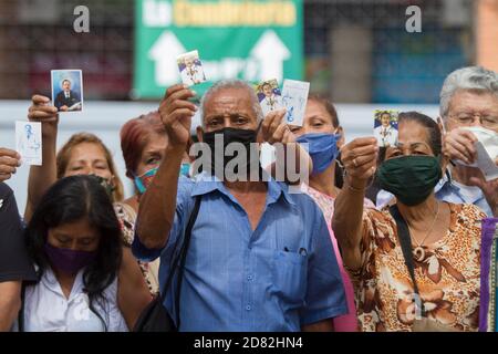 Caracas, Venezuela. Oktober 2020. Gläubige mit Mundschutz halten Bilder des venezolanischen Arztes Jose Gregorio Hernandez vor der Kirche "Nuestra Señora de la Candelaria", wo die Überreste des 1919 verstorbenen Arztes ausgegraben werden. Die Exhumierung, die in Anwesenheit von Zeugen stattfand, wurde im Rahmen des Prozesses zur Seligsprechung der Venezolaner durchgeführt. Hernandez wird von vielen Gläubigen im südamerikanischen Land verehrt. Kredit: Pedro Rances Mattey/dpa/Alamy Live Nachrichten Stockfoto