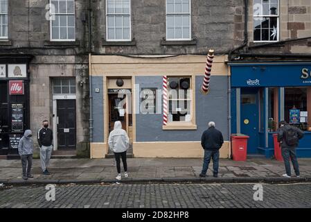 Sozial distanzierte Warteschlange vor dem James Wood & Sons Barber Shop, gegründet 1890, Drummond Street, Edinburgh, Schottland, Großbritannien. Stockfoto