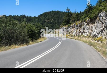 Kurvenreiche Straße Berg überquert Tannenwälder unter dem blauen klaren Himmel Stockfoto