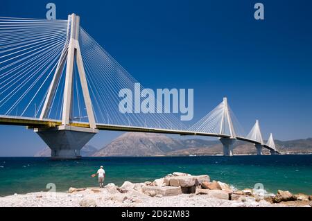 Ein Fischer, der unter der Hängebrücke über die Meerenge des Golfs von Korinth fischt, Griechenland. Stockfoto