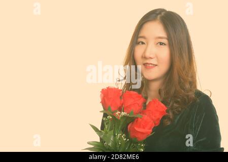 Junge, glückliche Asiatin, die rote Rosen zum Valentinstag hält Stockfoto