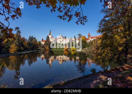 Pruhonice, Tschechische Republik - Oktober 25 2020: Blick auf die berühmte romantische Burg über einem See auf einem grünen Hügel im Park. Sonniger Herbsttag. Stockfoto