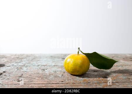 Eine Mandarine mit einem Blatt auf einer langen Holzbank an einer weißen Wand. Speicherplatz kopieren Stockfoto