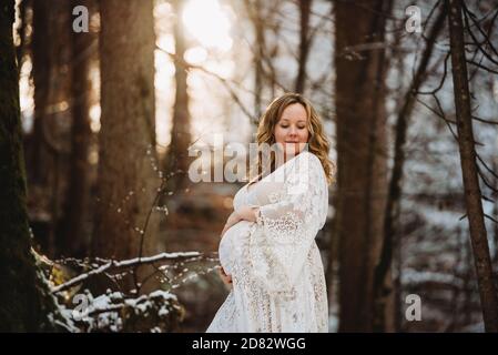 Schwangere Frau, die im Winter mit in den Wald schaut goldenes Licht Stockfoto