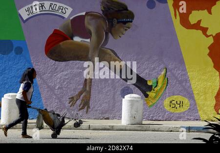 Valencia, Carabobo, Venezuela. Oktober 2020. Bildunterschrift: 26. Oktober 2020. Awoman, mit Wasser in einer Babykutsche läuft vor einem Graffiti des venezolanischen Athleten Yulimar Rojas, Olympiasiegerin in Rio 2016, Indoor-Weltmeister und Indoor-Weltrekordler in der Spezialität des weiblichen Dreisprungs. Dies ist eine Hommage des Bürgermeisters von Valencia, an die herausragenden Nachkommen des Afros. In Valencia, Carabobo, Venezuela - Foto: Juan Carlos Hernandez Kredit: Juan Carlos Hernandez/ZUMA Wire/Alamy Live News Stockfoto