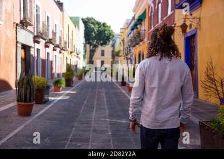 Mann mit lockigen Haaren, der auf der farbenfrohen Kolonialstraße von Puebla spazierengeht Stockfoto