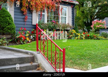 Ein leuchtend roter Metallhandlauf führt vier Betonstufen hinauf zu einem Gehweg. Stockfoto