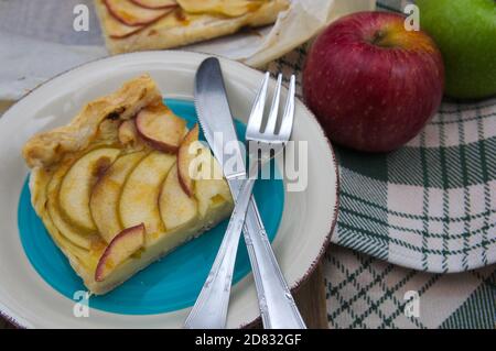 Teller serviert mit einer Scheibe Apfelkuchen mit Pudding neben zwei Äpfeln, einem roten und einem goldenen Stockfoto