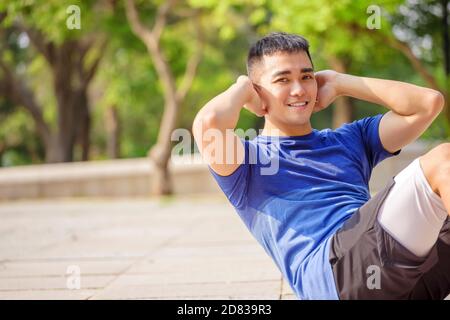 Junger Mann, der im Park Sit-ups trainiert und macht Stockfoto