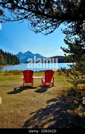 Ein vertikales Bild von zwei roten Stühlen, auf denen jemand sitzen und den Blick auf den Maligne Lake im Jasper National Park in Alberta, Kanada, genießen kann. Stockfoto