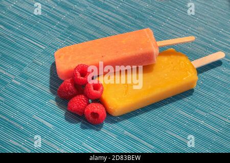 Fruchtpopsicles auf einem aquabluen Hintergrund im Sommer einschließlich Wassermelone Popsicle, tropische Frucht Popsicle, Mango Popsicle, und Limettenpopsicle mit Fr. Stockfoto