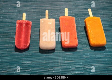 Fruchtpopsicles auf einem aquabluen Hintergrund im Sommer einschließlich Wassermelone Popsicle, tropische Frucht Popsicle, Mango Popsicle, und Limettenpopsicle mit Fr. Stockfoto