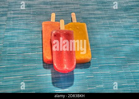 Fruchtpopsicles auf einem aquabluen Hintergrund im Sommer einschließlich Wassermelone Popsicle, tropische Frucht Popsicle, Mango Popsicle, und Limettenpopsicle mit Fr. Stockfoto