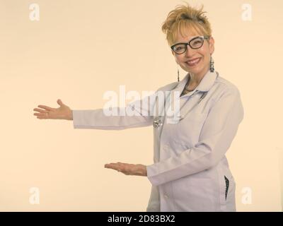 Studio Aufnahme von glücklich Senior asiatische Frau Arzt lächelnd während Etwas zeigen und Brillen tragen Stockfoto