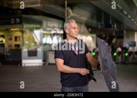 Schöner persischer Mann, der am Bahnhof des Skytrain Regenschirm öffnet Stockfoto