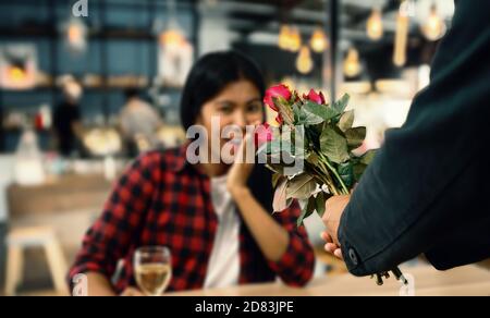 Pärchen beim Abendessen in einem Restaurant, Frauen in rot-schwarz gestreiften Hemden der Mann trägt einen schwarzen Anzug, er gibt seiner Freundin eine rote Rose Stockfoto