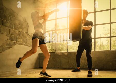 Asia Frau in einem Fitness-Anzug tritt einen Sandsack in die Turnhalle und der Trainer ist der Sandbag-Catcher. Stockfoto