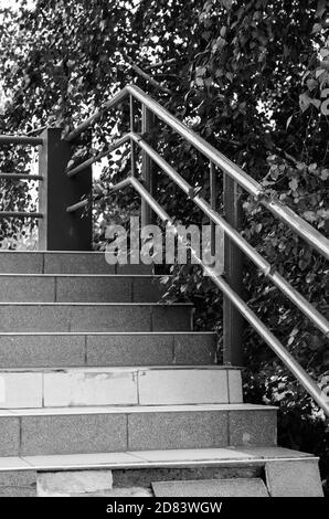 Treppe mit Geländer draußen. Schwarz-Weiß-Foto einer Steintreppe mit Metallgeländer. Ohne irgendjemanden. Stockfoto