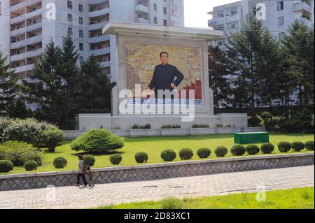 08.08.2012, Pjöngjang, Nordkorea, Asien - eine alltägliche Straßenszene zeigt ein Denkmal mit dem Porträt von Kim Il Sung und Wohngebäuden. Stockfoto