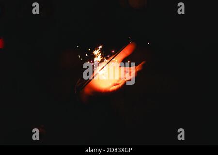 Funken und Licht von Wunderkerzen im Dunkeln auf der Handfläche einer Person. Weihnachtszauber, Silvester, festlicher Hintergrund. Leerzeichen für Text Stockfoto