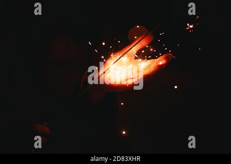 Funken und Licht von Wunderkerzen im Dunkeln auf der Handfläche einer Person. Weihnachtszauber, Silvester, festlicher Hintergrund. Leerzeichen für Text Stockfoto