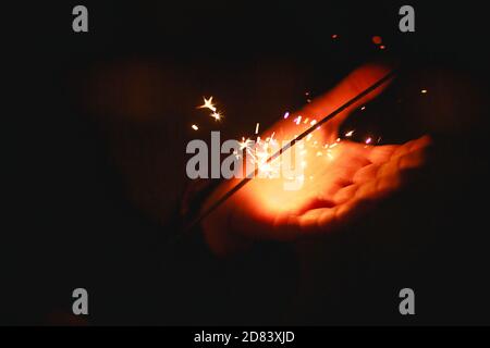 Funken und Licht von Wunderkerzen im Dunkeln auf der Handfläche einer Person. Weihnachtszauber, Silvester, festlicher Hintergrund. Leerzeichen für Text Stockfoto