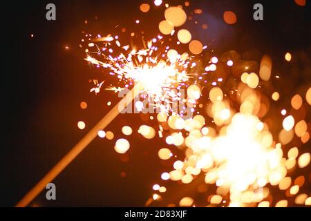 Funken und Licht von Wunderkerzen im Dunkeln mit hellem Gelb und Orange Bokeh und Rauch. Festliche Feuer Textur, Hintergrund für Neujahr und Weihnachten Stockfoto