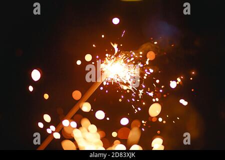 Funken und Licht von Wunderkerzen im Dunkeln mit hellem Gelb und Orange Bokeh und Rauch. Festliche Feuer Textur, Hintergrund für Neujahr und Weihnachten Stockfoto