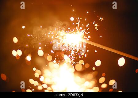 Funken und Licht von Wunderkerzen im Dunkeln mit hellem Gelb und Orange Bokeh und Rauch. Festliche Feuer Textur, Hintergrund für Neujahr und Weihnachten Stockfoto
