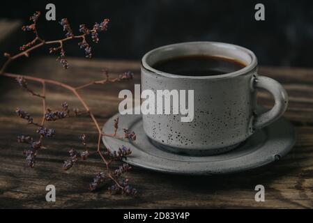Eine Tasse Espresso auf einem Holztisch auf dunklem Hintergrund. Ein Zweig getrockneter Blumen in der Nähe. Stockfoto