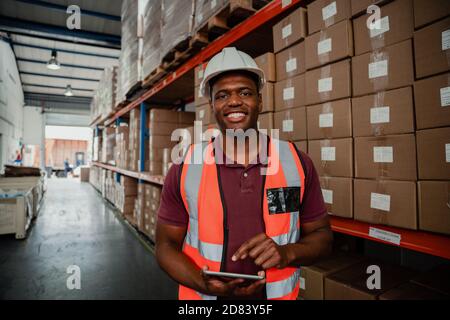 Lächelnd ethnischen männlichen Geschäftsmann Organisation Versandinformationen auf digitalen Tablet im Lager stehen. Stockfoto
