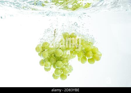 Frische weiße Muskattrauben fallen ins Wasser, isoliert auf weißem Hintergrund Stockfoto