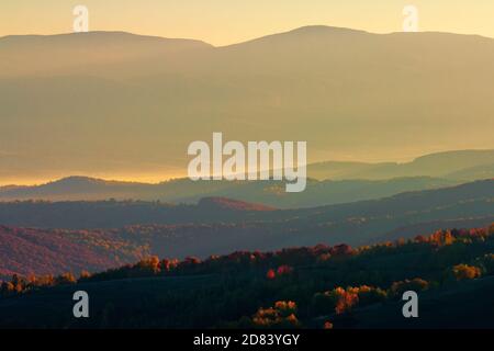 Misty Sonnenaufgang in den Bergen. schöne Herbstwetter. schöne Natur Landschaft vom Gipfel eines Hügels beobachtet. Bäume in bunten Herbstfarben. Nebel gl Stockfoto
