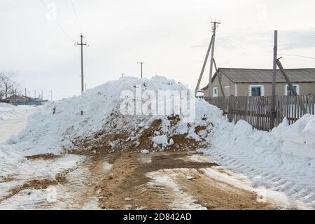 Die Straße im Dorf ist schneefrei und mit Sand bedeckt für sicheren Verkehr. Schnee driftet entlang der Straße Stockfoto