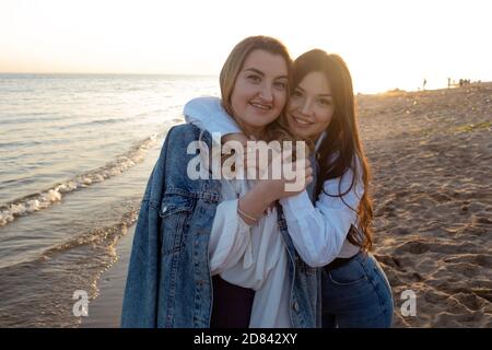 Freunde haben eine glückliche Zeit zusammen. Junge Frauen am Strand am Abend, umarmend und lachend. Stockfoto