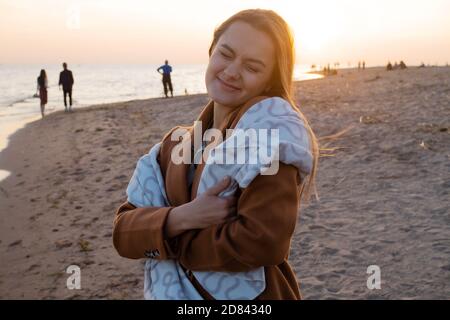 Junge schöne Frau in eine warme Decke eingewickelt, warm und gemütlich am Strand. Am Strand bei Sonnenuntergang laufen, sich frei und glücklich fühlen. Stockfoto