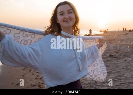 Junge schöne Frau in eine warme Decke eingewickelt, warm und gemütlich am Strand. Am Strand bei Sonnenuntergang laufen, sich frei und glücklich fühlen. Stockfoto