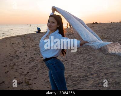 Junge schöne Frau in eine warme Decke eingewickelt, warm und gemütlich am Strand. Am Strand bei Sonnenuntergang laufen, sich frei und glücklich fühlen. Stockfoto