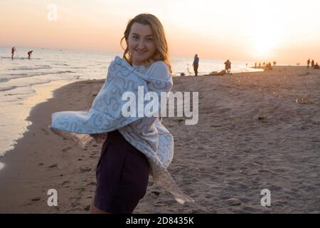 Junge schöne Frau in eine warme Decke eingewickelt, warm und gemütlich am Strand. Am Strand bei Sonnenuntergang laufen, sich frei und glücklich fühlen. Stockfoto