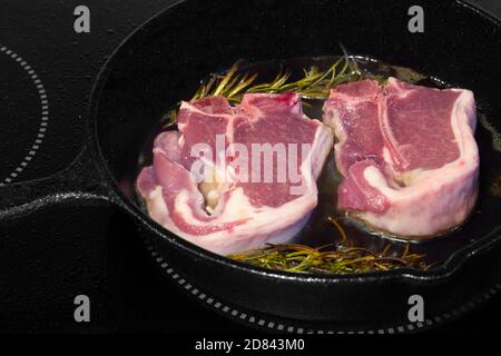 Lammkoteletts mit Rosmarin in einer gusseisernen Pfanne. Kochen auf einem Elektroherd Stockfoto