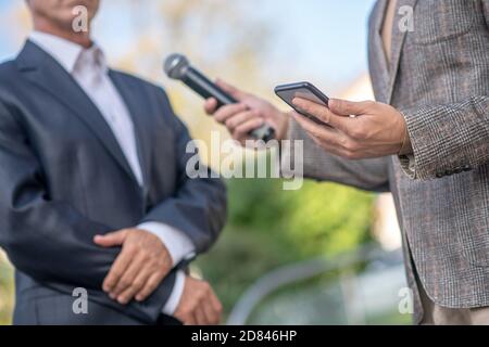 Nahaufnahme der männlichen Hände mit Mikrofon und Smartphone, Aufnahme Interview Stockfoto