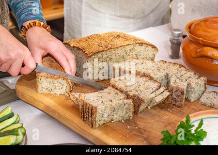 Hausgemachtes braun duftendes frisches Getreide Brot auf einem rustikalen Holzbrett mit einer Frau hält Messer für Schnitt, Nahaufnahme Stockfoto