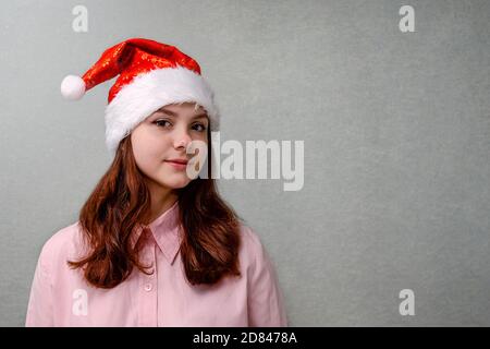 Ein Mädchen im Teenageralter steht zu Hause in einem Weihnachtsmann hut und Lächeln Stockfoto