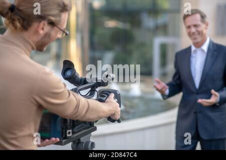 Der blonde Fahrer filmt draußen vor dem Hotel einen reifen männlichen Bericht Stockfoto