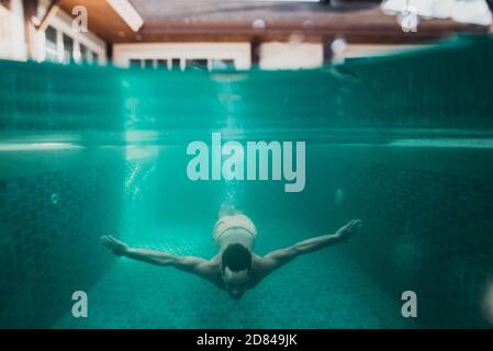 Mann schwimmend im Pool unter Wasser, in seinem schönen Ferienhaus Stockfoto