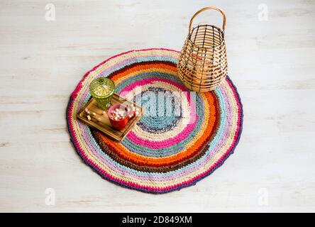 Bunte Häkeldecke, Upcycling aus geschnittenen umfunktionierten T-Shirts auf weißem Holzboden mit Holzlaterne, Kerzenbrennen. Tasse auf heißer Schokolade. Stockfoto